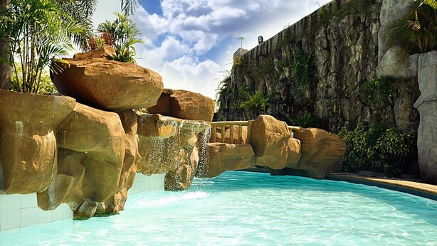 A pool with clear water, surrounded by large rocks and a rocky cliff.