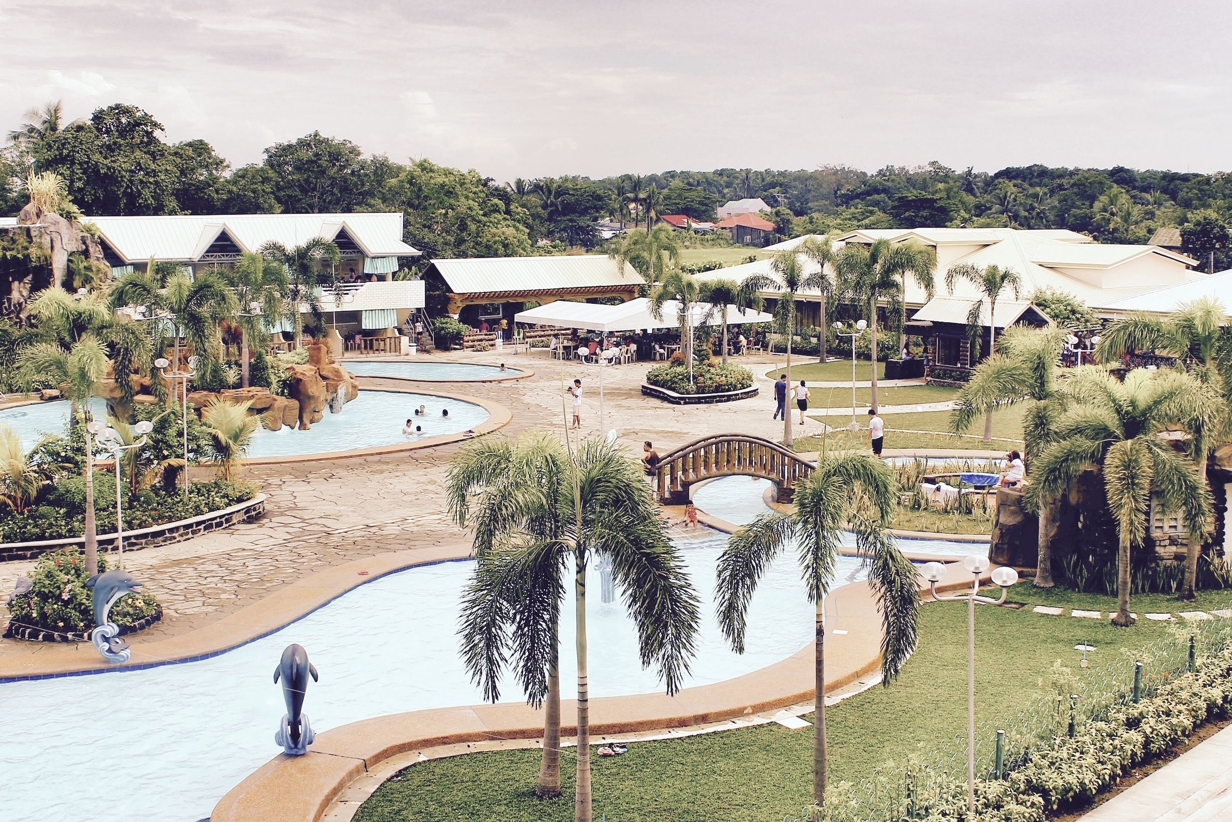 Un resort con varias piscinas, palmeras y un puente que conecta diferentes zonas.
