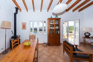 Zona pranzo con tavolo in legno, sedie, credenza con stoviglie e vista dalle finestre.