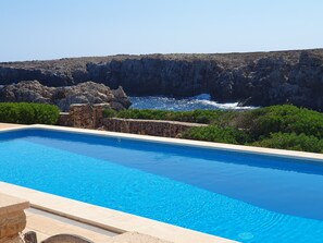 A swimming pool with clear blue water, surrounded by rocky cliffs and greenery.