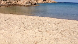 Una playa con agua cristalina y una ladera rocosa.
