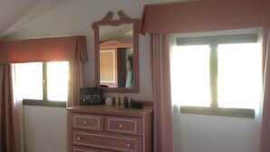 Un dormitorio con un aparador, un espejo y dos ventanas con cortinas.
