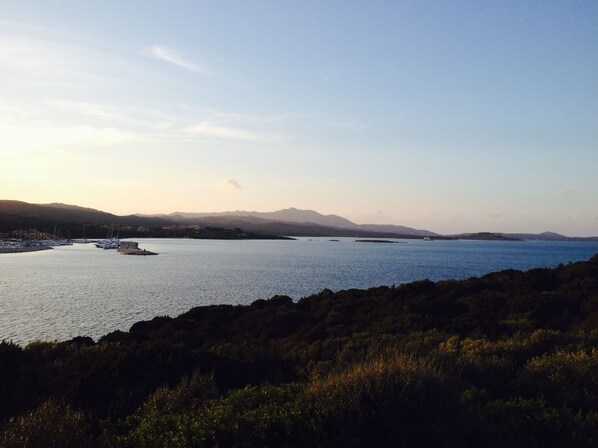 A coastal landscape with boats docked near the shore, a clear sky, and distant mountains.