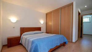 A bedroom with a wooden bed, a nightstand, a wardrobe, and two wall-mounted lights. - Casa do Pioledo (Camélias de Basto-Turismo Rural) (Celorico de Basto)