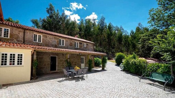 A stone building with a tiled roof, a paved courtyard, and a table with chairs. - Casa do Pioledo (Camélias de Basto-Turismo Rural) (Celorico de Basto)