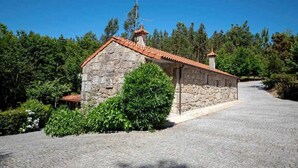 A stone building with a tiled roof, surrounded by greenery and a cobblestone path. - Casa do Pioledo (Camélias de Basto-Turismo Rural) (Celorico de Basto)