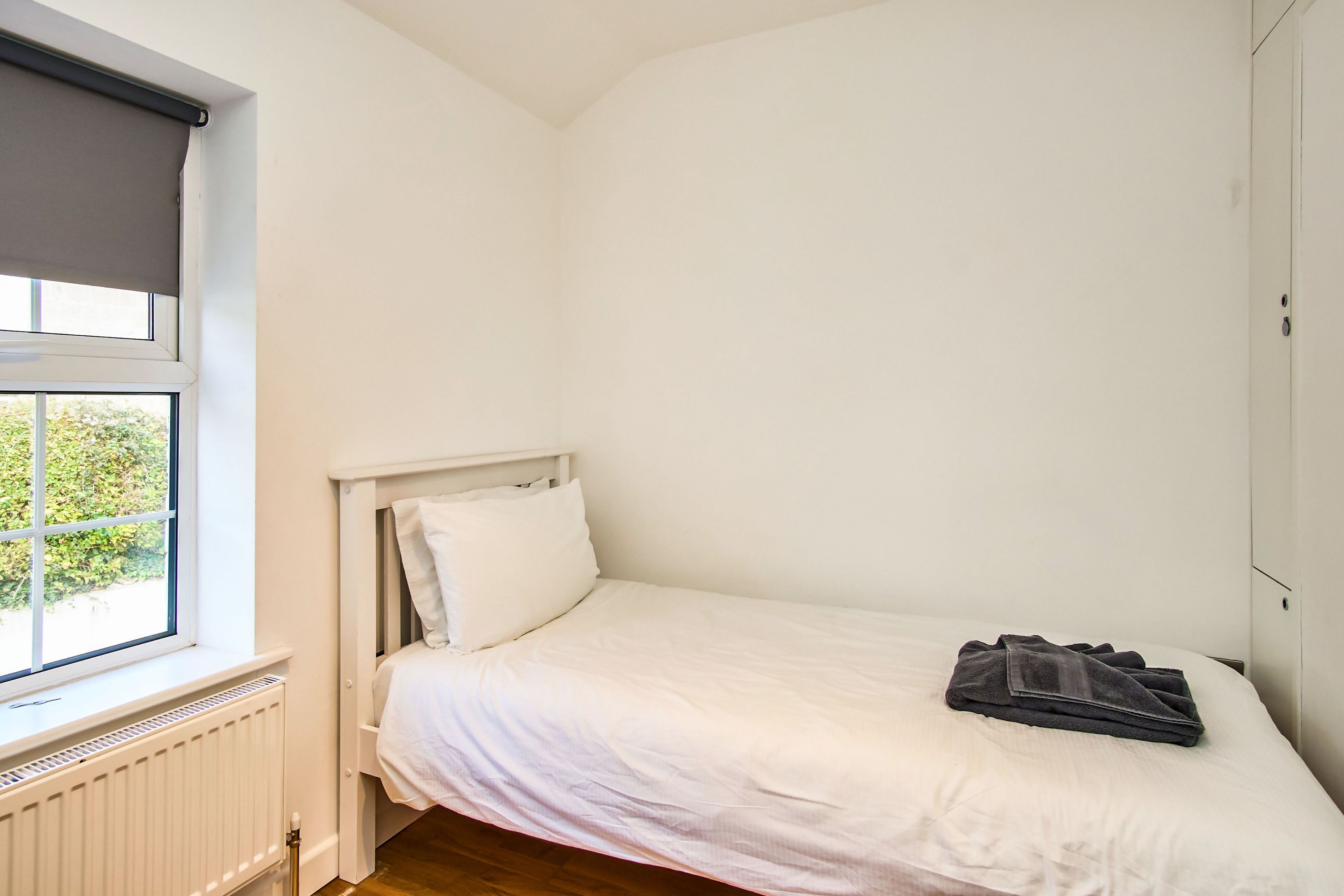 Una habitación pequeña con cama individual, ventana, paredes blancas y radiador.