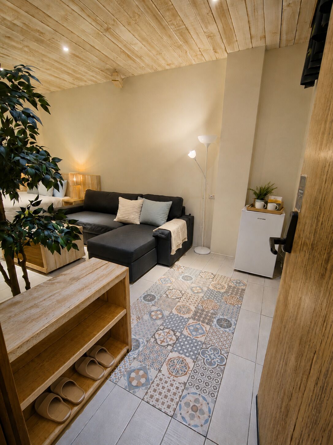 A cozy living area with a sofa, a coffee table, a floor lamp, and a small refrigerator.