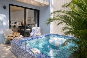 Un área de piscina privada con suelo de baldosas, sillas de descanso, un aro flotante y una planta en maceta.