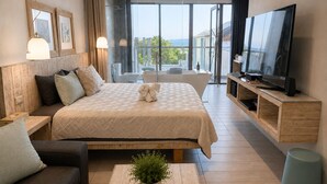 A modern hotel room with a large bed, a TV, a sofa, a small table with a plant, and a view of the outdoors. - Azure Inn (Hengchun)