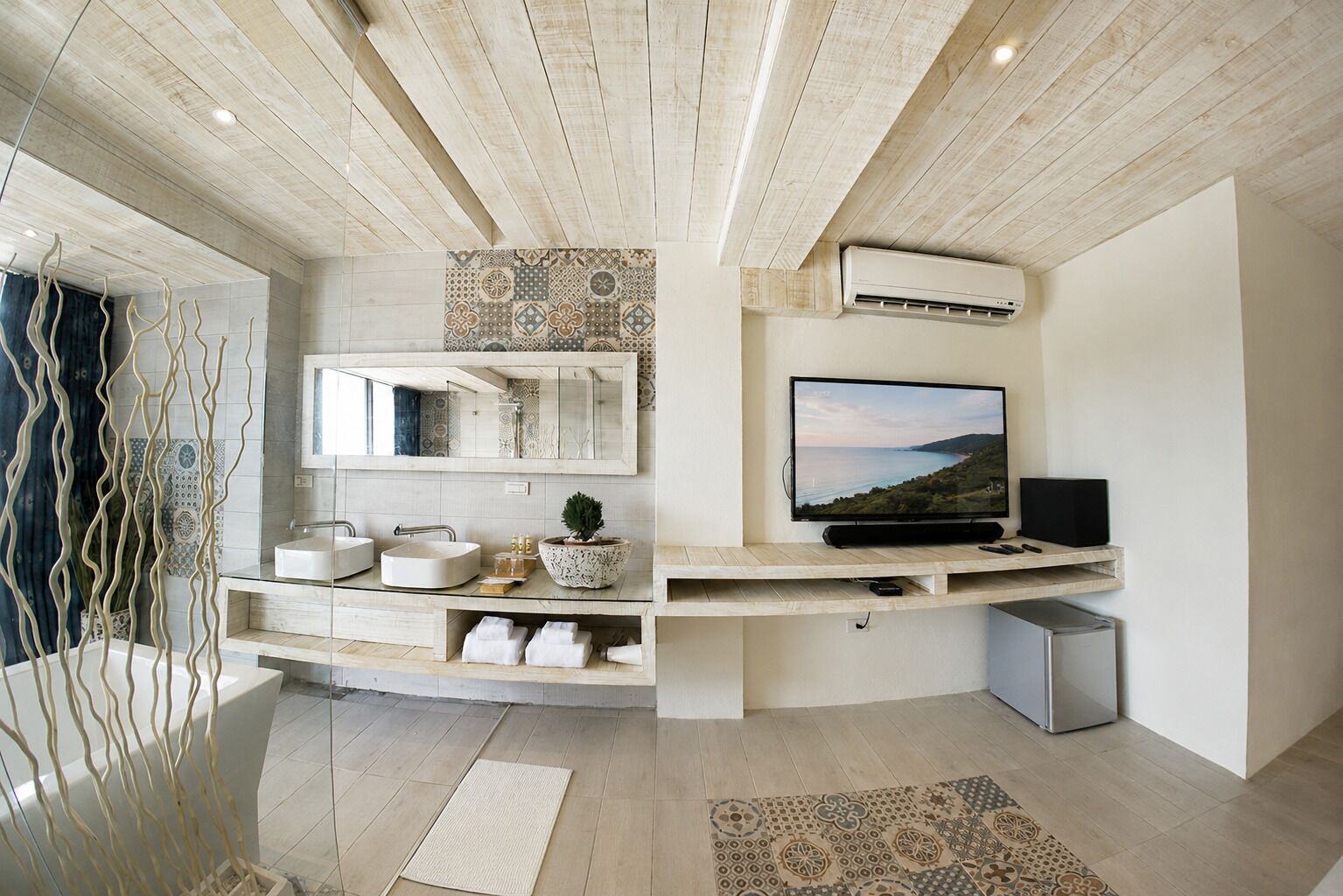 A modern bathroom with a vanity, sink, mirror, and a television on a wooden shelf.