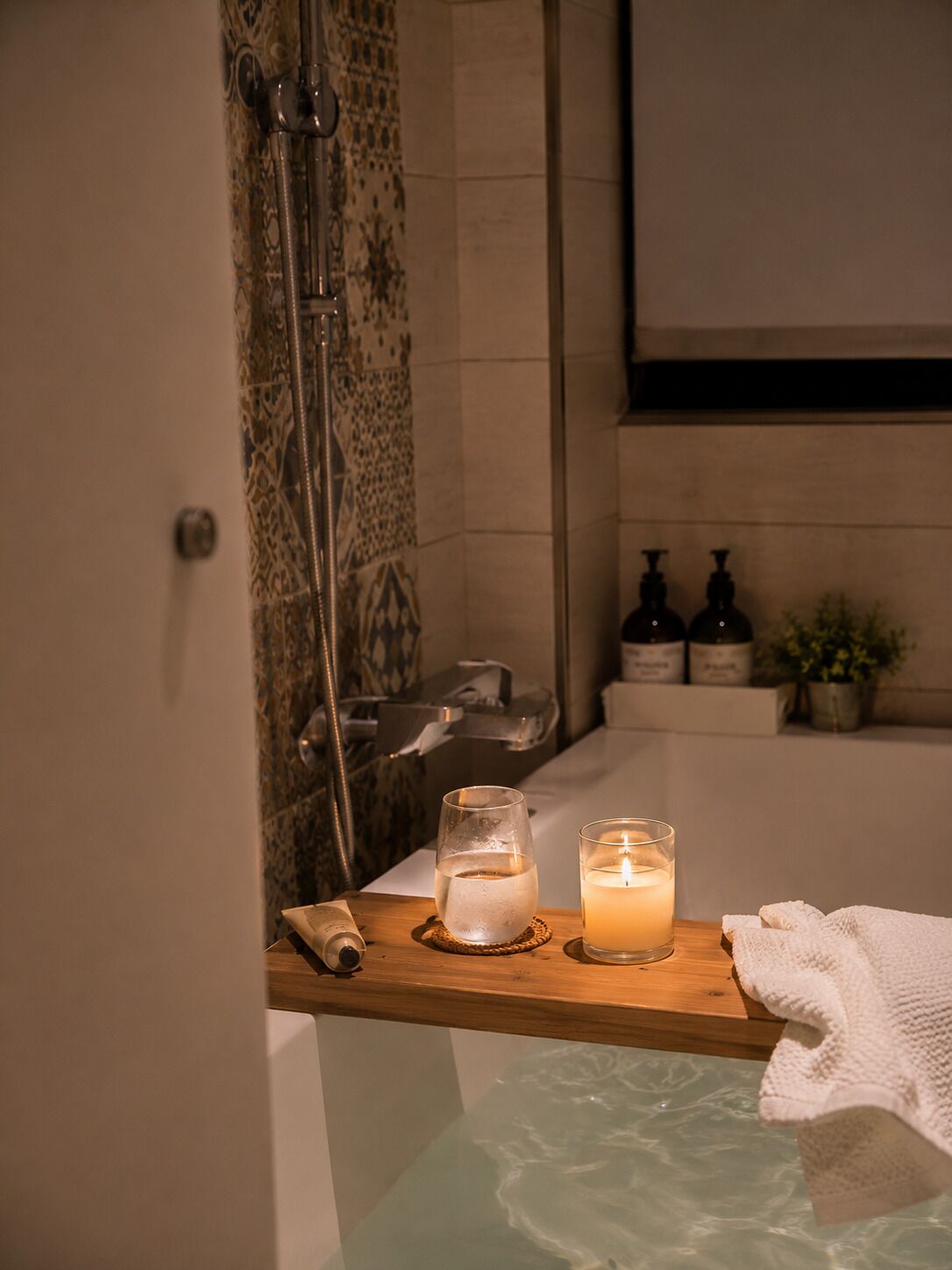 A bathroom with a shower, a bathtub, a wooden shelf with a candle, a glass of water, and toiletries.