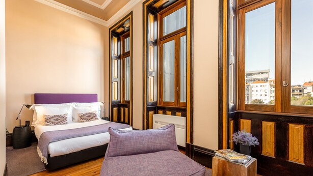 Ein Schlafzimmer mit Bett, Sofa, Nachttisch und Fenster mit Blick auf Gebäude.