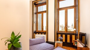 Ein Zimmer mit großem Fenster, einer Couch, einem kleinen Tisch und einem Fernseher.