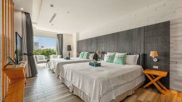 A hotel room with two beds, a TV, a desk, and a view of greenery outside.