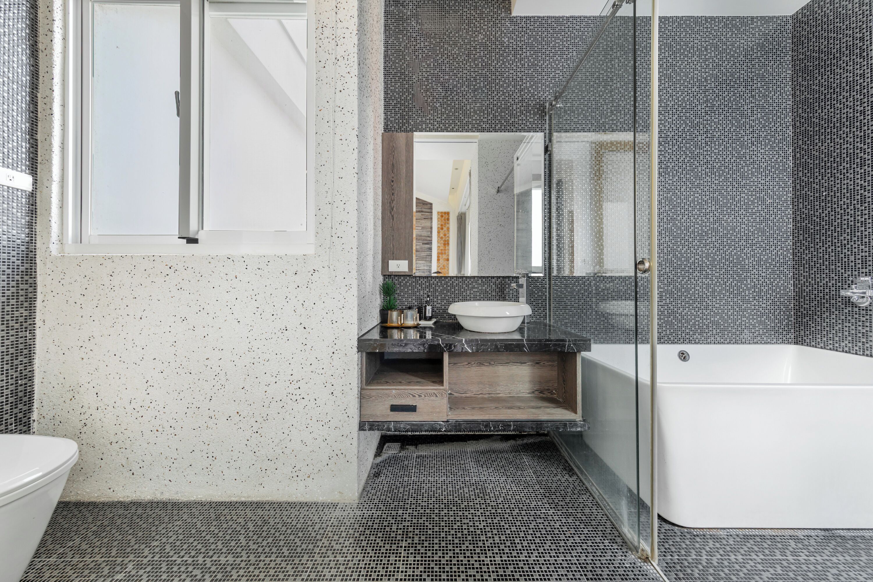 Une salle de bain moderne avec une baignoire sur pieds, une douche à parois de verre et un lavabo blanc posé sur un plan de travail foncé.
