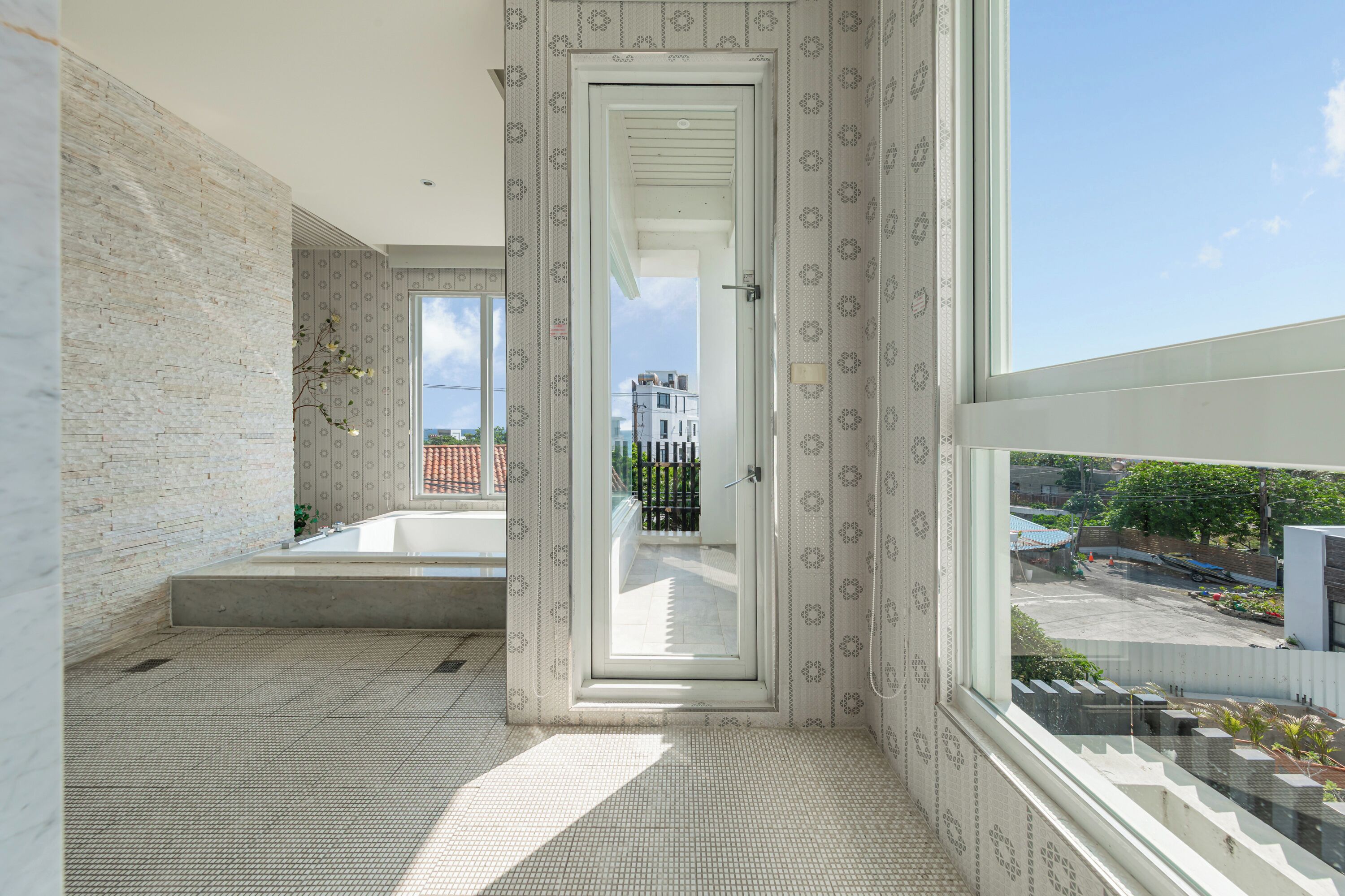 Une salle de bain moderne dotée d’une grande fenêtre, d’une baignoire et offrant une vue sur un immeuble et la verdure environnante.