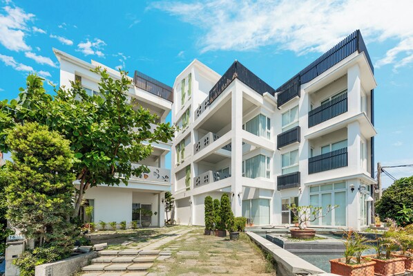 A modern multi-story building with balconies, a courtyard with potted plants, and a clear blue sky. - Zen Pin Inn (Hengchun)