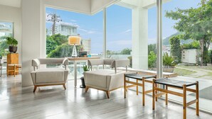Un vaste espace de vie comprenant un canapé moderne, une table à manger et des chaises, ainsi que de grandes fenêtres offrant une vue sur la ville et la verdure.