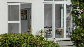 Ein modernes Gebäude mit großen Glasfenstern und -türen, ein sichtbarer Innenbereich mit Essbereich sowie ein gepflegter Garten mit roten Blüten.