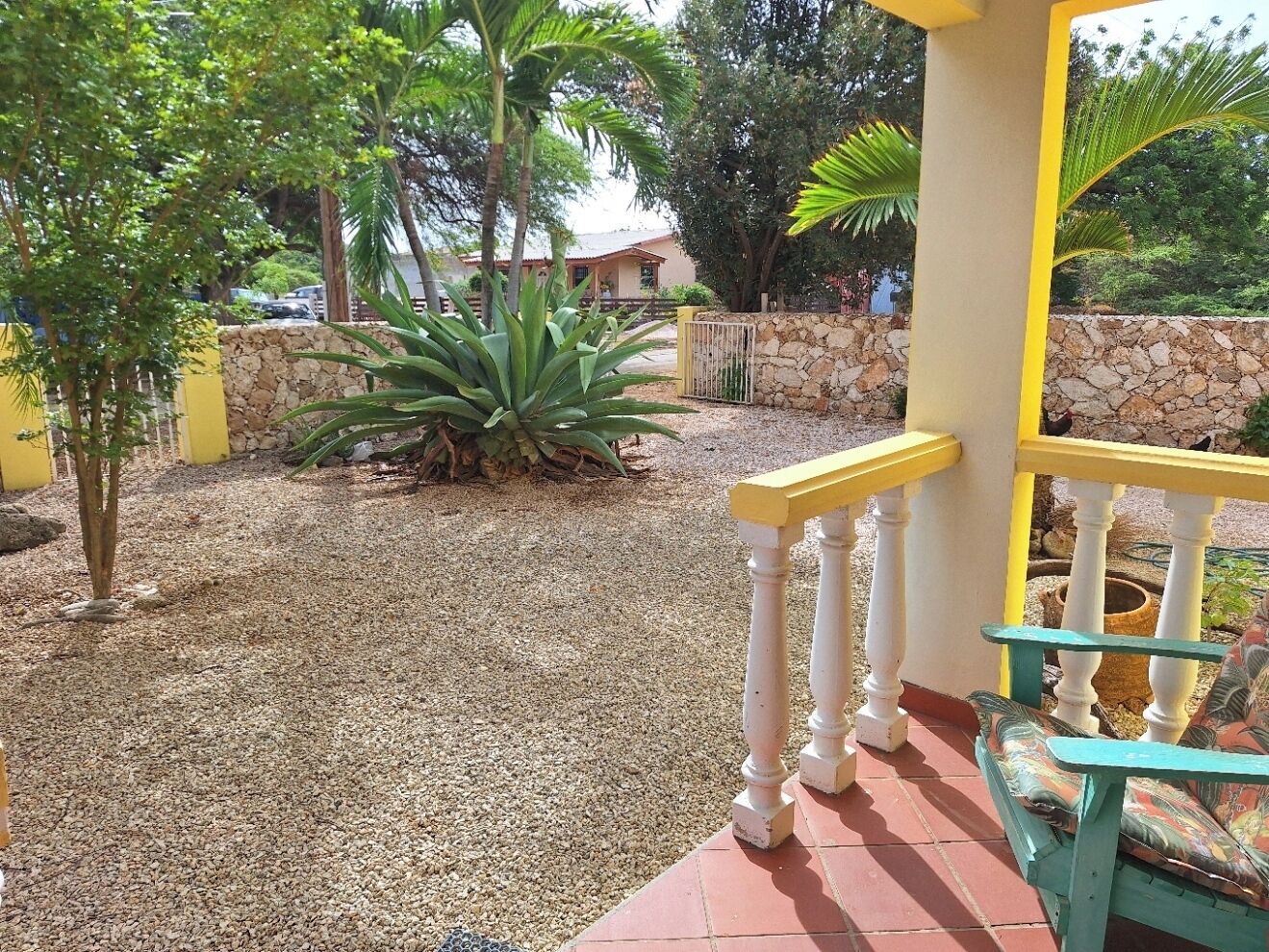 A covered outdoor area with a gravel path, a stone wall, and a yellow railing.