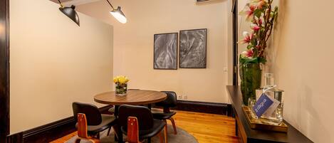 A dining area with a round table, four chairs, a vase with flowers, and two framed artworks on the wall.