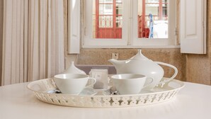 A table with white teaware set on a tray, a window with red shutters, and a beige wall.