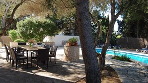 An outdoor patio with a dining table and chairs, a stone pool, and surrounding greenery. - Lovely holiday villa. Pool and beach (Cala Serena)