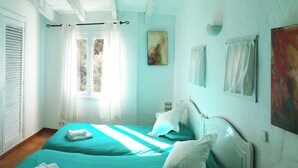 A bedroom with two beds, a window with curtains, a painting on the wall, and a radiator. - Lovely holiday villa. Pool and beach (Cala Serena)