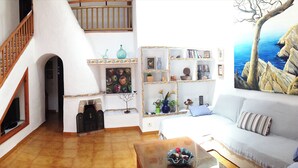 A living room with a staircase, a fireplace, a bookshelf, and a painting of a tree. - Lovely holiday villa. Pool and beach (Cala Serena)