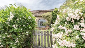 A garden with a wooden fence, lush greenery, and a building with a tiled roof. - House with pool. Idyllic setting in hills near Lucca and coast WiFi Aircon       (Torcigliano)