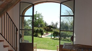 A room with a large arched window leading to a garden with a pool and outdoor furniture. - House with pool. Idyllic setting in hills near Lucca and coast WiFi Aircon       (Torcigliano)