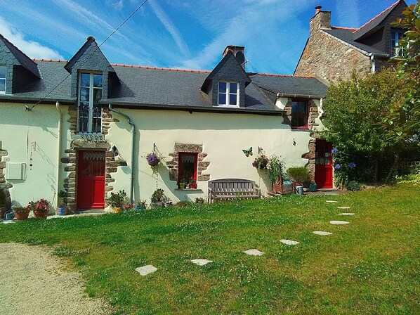 A traditional stone house with a red door, multiple windows, and a well-maintained garden. - Charming cottage with enclosed garden in peaceful countryside. Pet welcome. (Béganne)