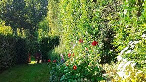 Ein weißer Hund liegt im Garten auf Gras, umgeben von verschiedenen Pflanzen und Blumen.