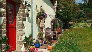 Ein charmantes Steinhaus mit roter Tür, Außenbestuhlung und Blumentöpfen.
