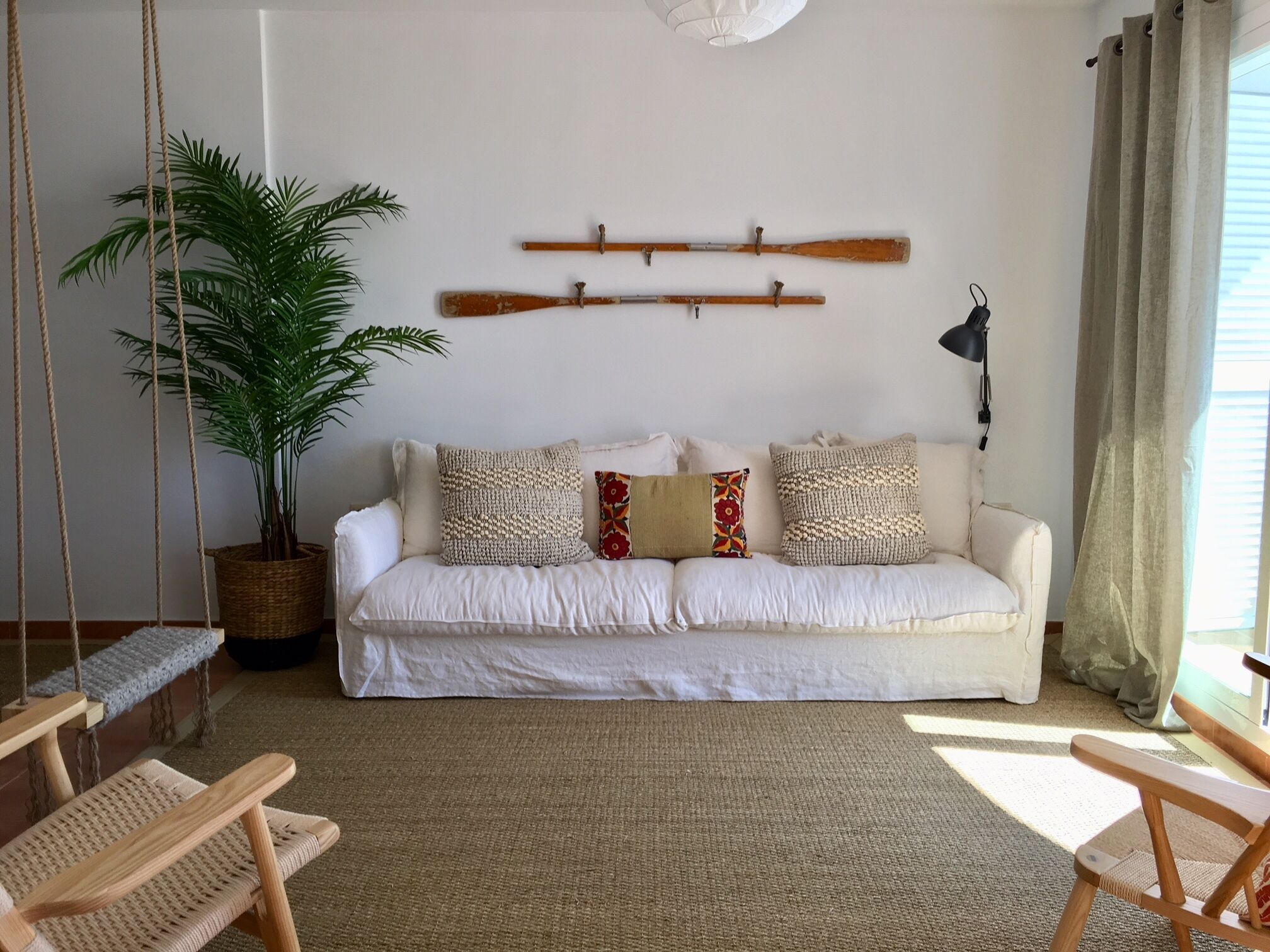 A living room with a white sofa, a potted plant, a hanging swing, and a wooden bench.