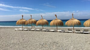 Une plage bordée de parasols en chaume et de chaises longues blanches, alignées le long du rivage.