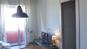 Una habitación con una mesa de comedor de madera, un televisor sobre un soporte, una lámpara y un equipo de aire acondicionado.