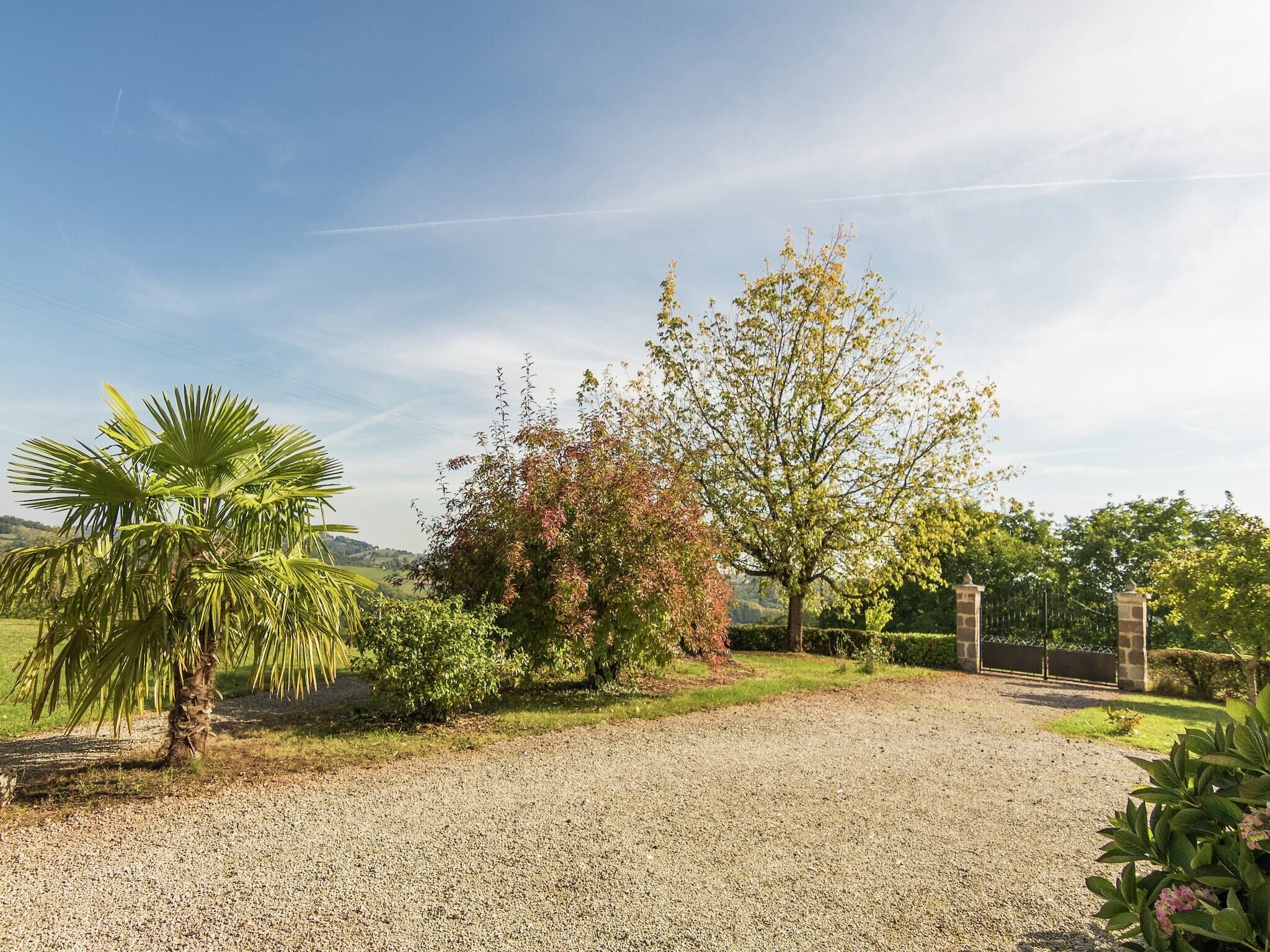 A gravel driveway leading to a stone gate, surrounded by lush greenery and trees.
