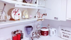 A kitchen with white cabinets, shelves with decorative plates, a kettle, and a coffee maker.