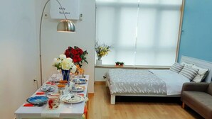 A room with a dining table set for a meal, a bed with a white bedspread, and a window with blinds.