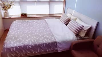 A neatly made bed with patterned bedding, a brown armchair, and a window with a view of the sky.