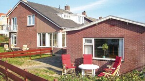 Et murstenshus med balkon, lille terrasse med røde stole og et bord, samt et stort vindue med en plante indeni.