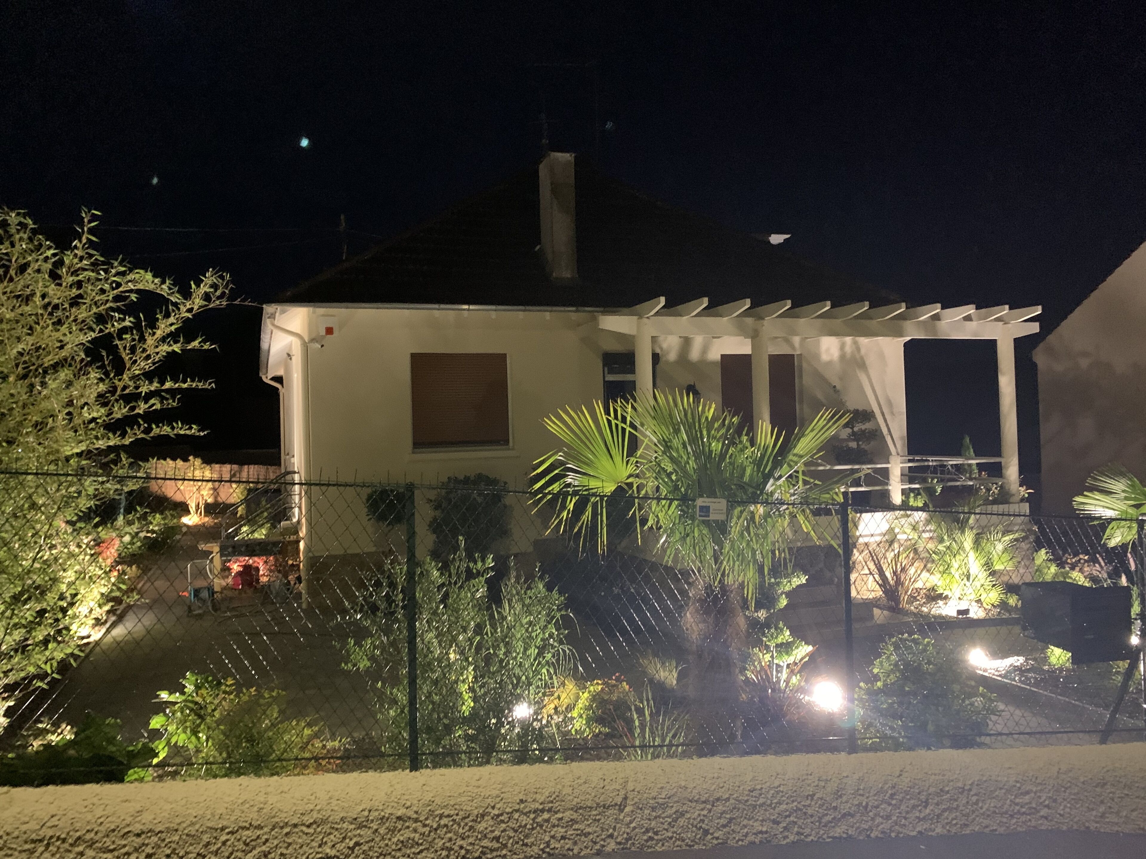 A house with a covered patio, surrounded by a fence and various plants.