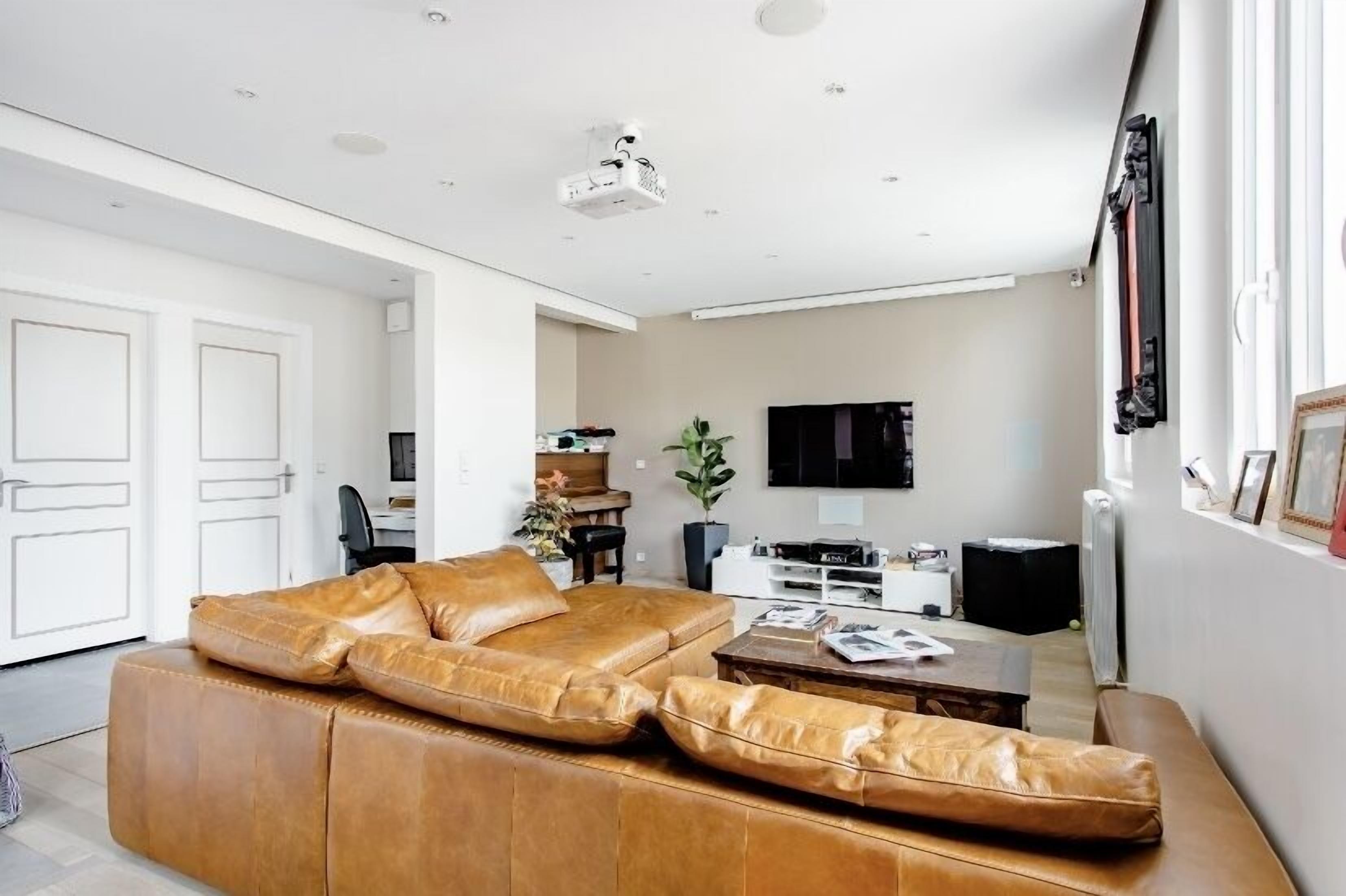 A modern living room with a brown leather sofa, a coffee table, a flat-screen TV, and a potted plant.