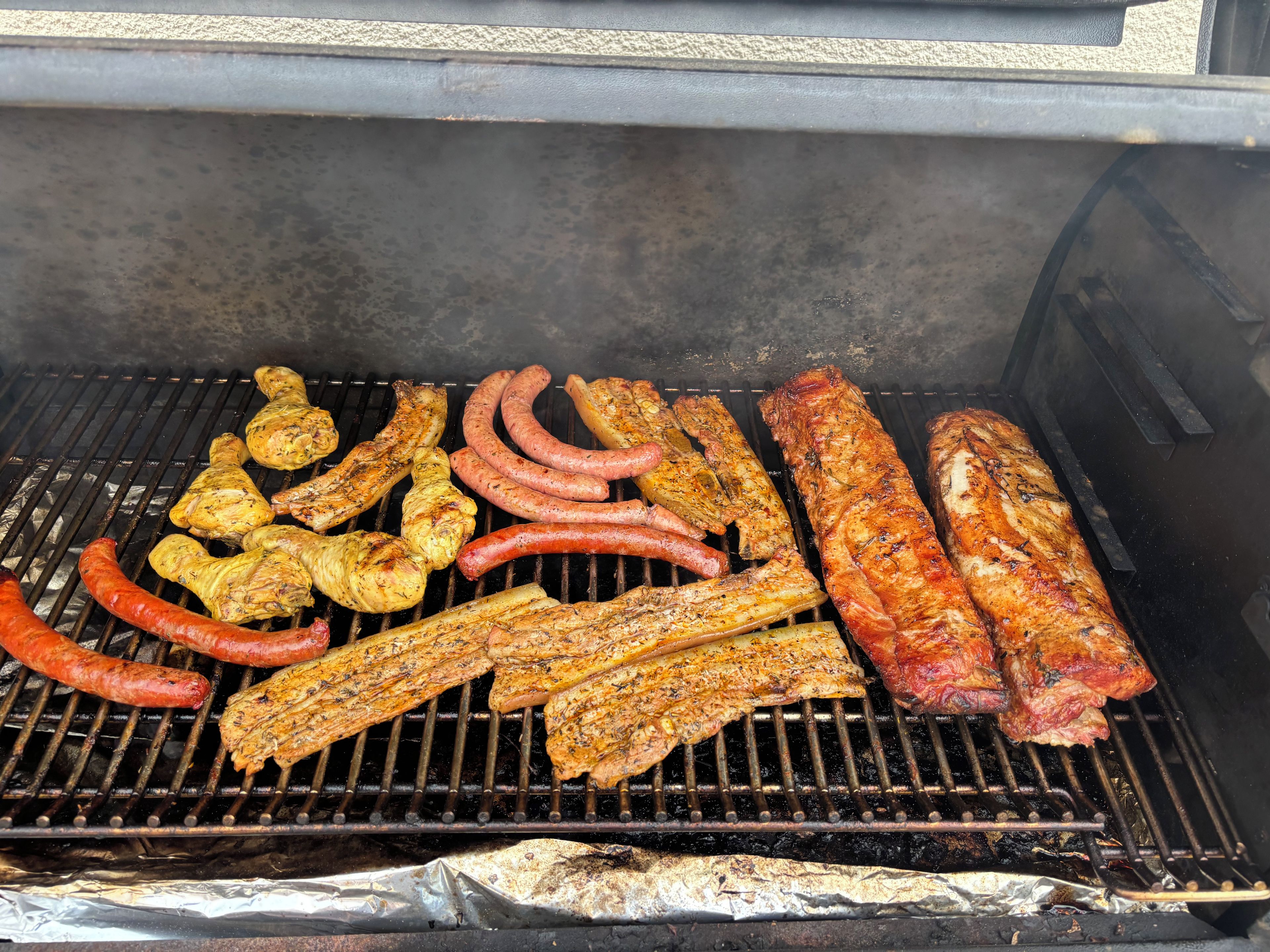 Ein Grill mit verschiedenen Fleischsorten und Gemüse, das zubereitet wird.