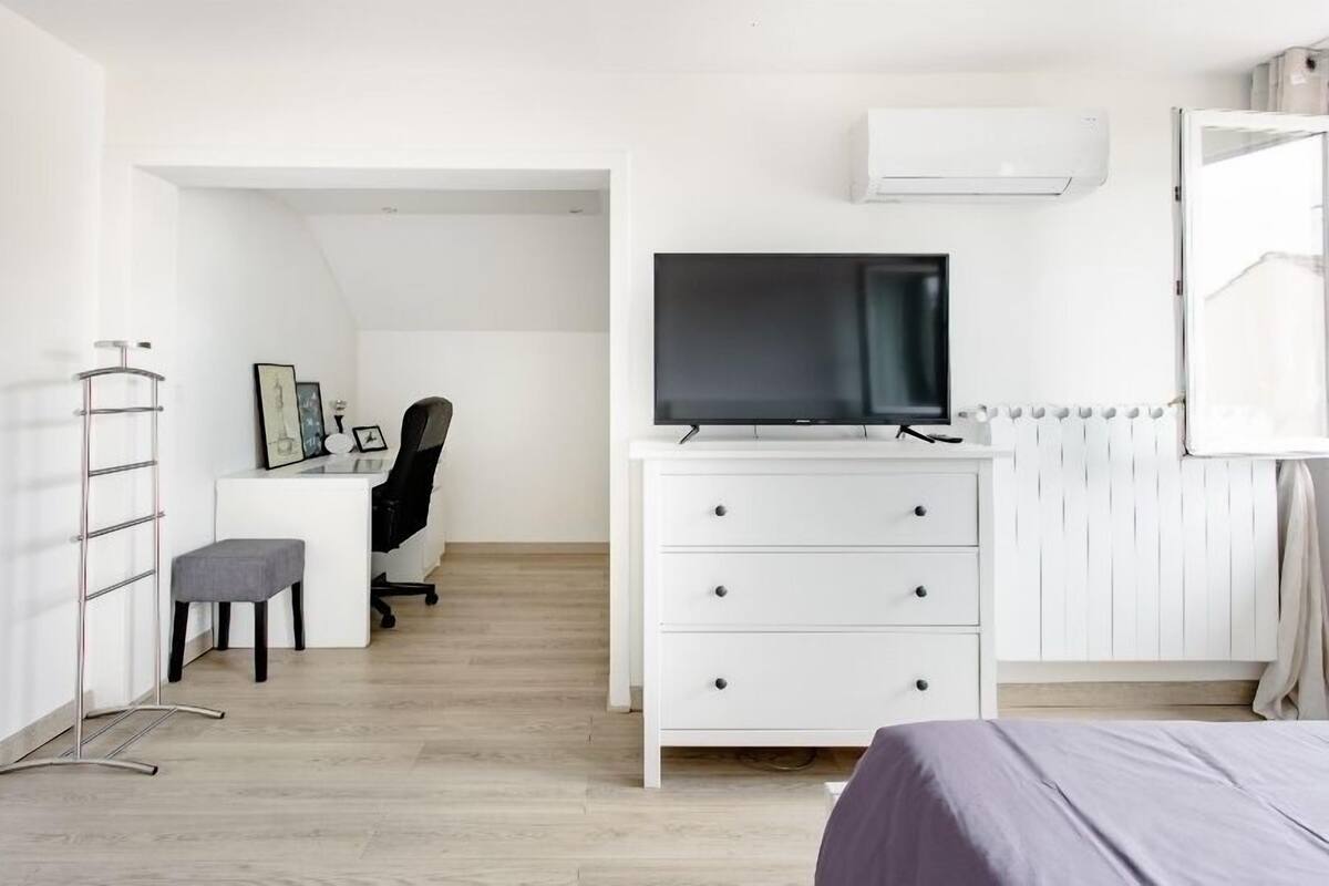 Et moderne soveværelse med seng, skrivebord med stol, fjernsyn og radiator.
