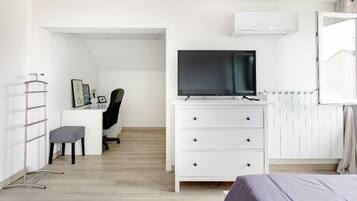Een moderne slaapkamer met een bed, een bureau met stoel, een televisie en een radiator.