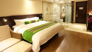 Una habitación de hotel moderna con una cama grande, una zona de estar separada, cabina de ducha con paredes de vidrio y suelo de madera.