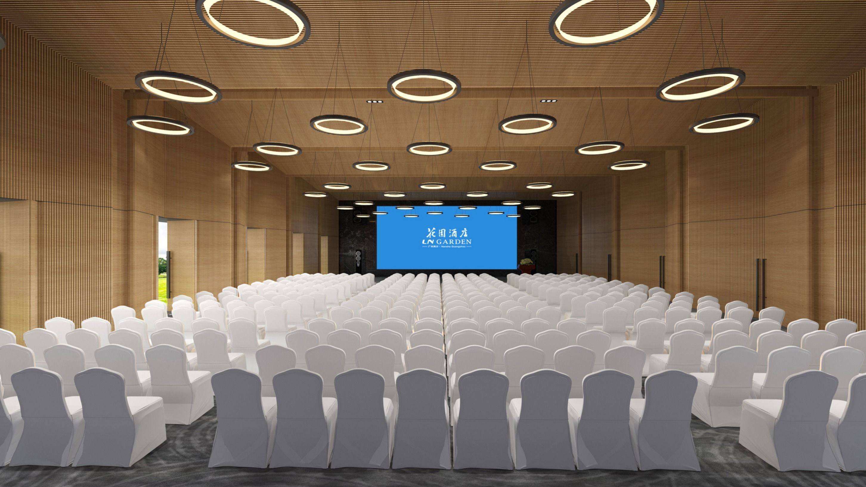 Un salón de conferencias con filas de sillas blancas, una pantalla grande al frente y luces circulares en el techo.